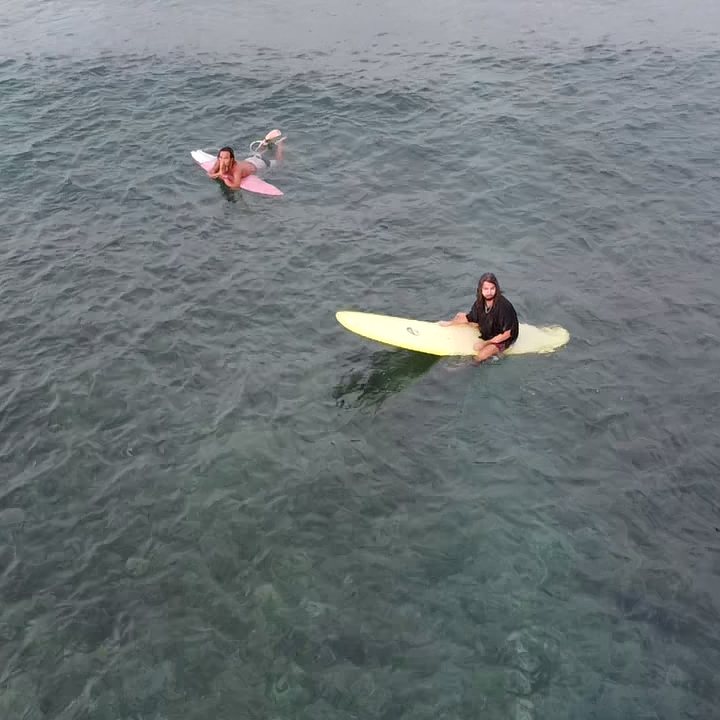 A surfer paddling into a small clean wave, seen from above