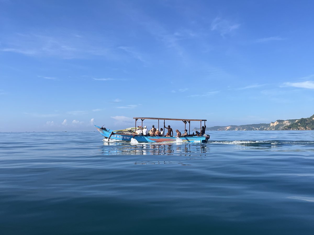 The boat out on flat water with the crew aboard, a board nose in the foreground